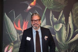 Mann mit Brille und Anzug steht vor einer bunten Pflanzenwand.