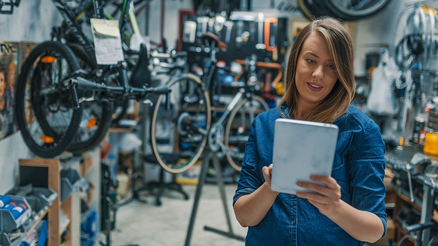 Frau nutzt Tablet in Fahrradwerkstatt: Digitalisierung auch in KMUs.