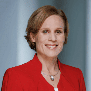 Porträt einer lächelnden Frau mit kurzen, blonden Haaren, die einen roten Blazer trägt.