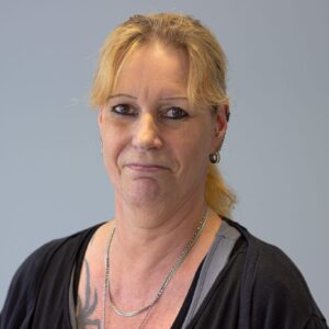 IMG_2575 Porträt einer Frau mit blonden Haaren, die in die Kamera schaut, vor einem grauen Hintergrund.