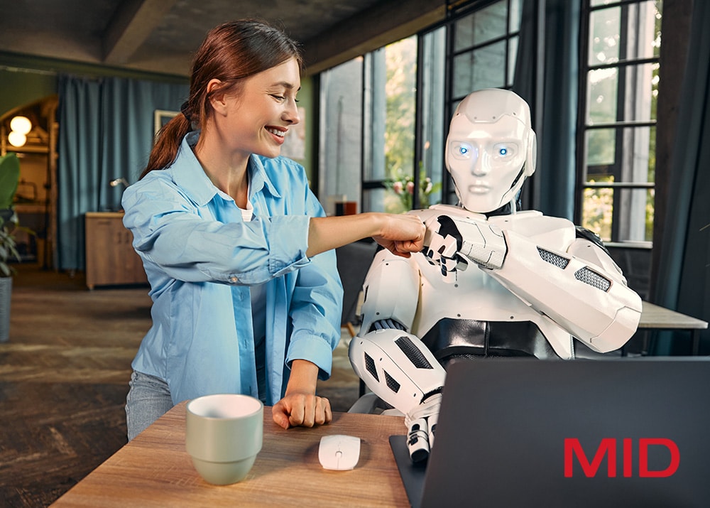 Frau mit blauen Hemd gibt einem humanoiden Roboter einen Fistbump an einem Tisch mit Laptop und Kaffeetasse.