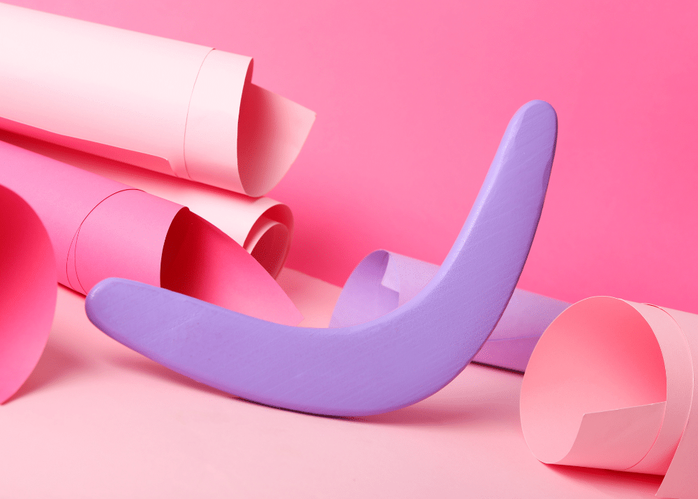 Lila gebogene Form liegt auf pinkem Hintergrund, umgeben von rosa Papierrollen.