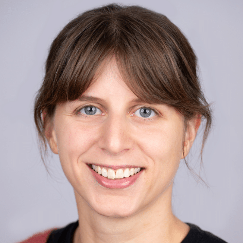 Porträt einer lächelnden Frau mit braunen Haaren und blauen Augen vor einem hellen Hintergrund.