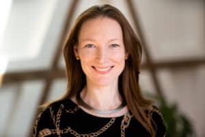 Svea-von-Hehn Porträt einer lächelnden Frau mit langen, braunen Haaren, die eine schwarze Bluse und eine silberne Halskette trägt.