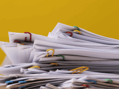 Stapel von Dokumenten mit bunten Büroklammern vor einem gelben Hintergrund.