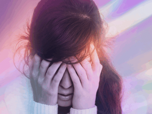 Frau mit geschlossenen Augen und Händen im Gesicht, umgeben von bunten Lichtstrahlen.