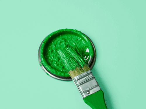 Ein Pinsel liegt in einer offenen Dose mit grüner Farbe auf einem mintgrünen Hintergrund.