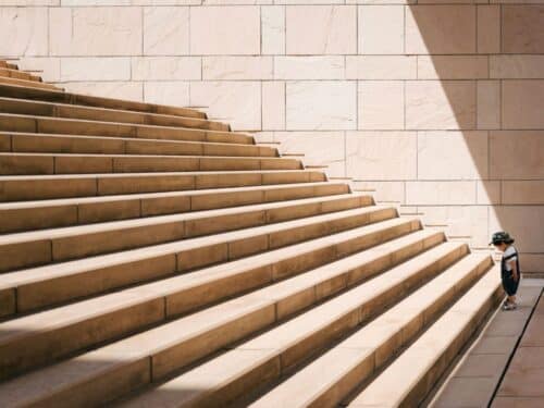 Ein Kind steht an der Seite einer breiten Treppe aus hellen Steinen, die in sanften Stufen angeordnet ist.
