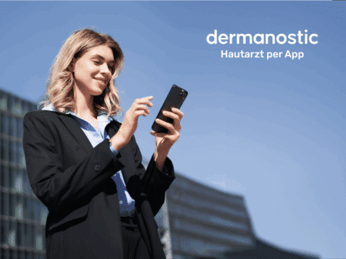 Frau in Anzug hält Smartphone, lächelt. Hintergrund zeigt moderne Gebäude. Text: "dermanostic Hautarzt per App".