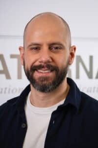 Stefan Schaus Porträt eines Mannes mit kurzem, glattem Haar und Bart, lächelnd vor einem neutralen Hintergrund.