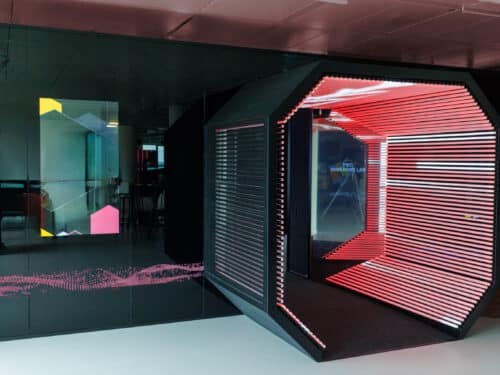 Futuristischer Raum mit einem hexagonalen Eingang, beleuchtet in Rot und Pink, umgeben von modernen, grafischen Elementen.