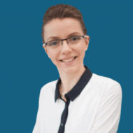 Frau mit Brille und bluse, lächelt vor einem blauen Hintergrund.