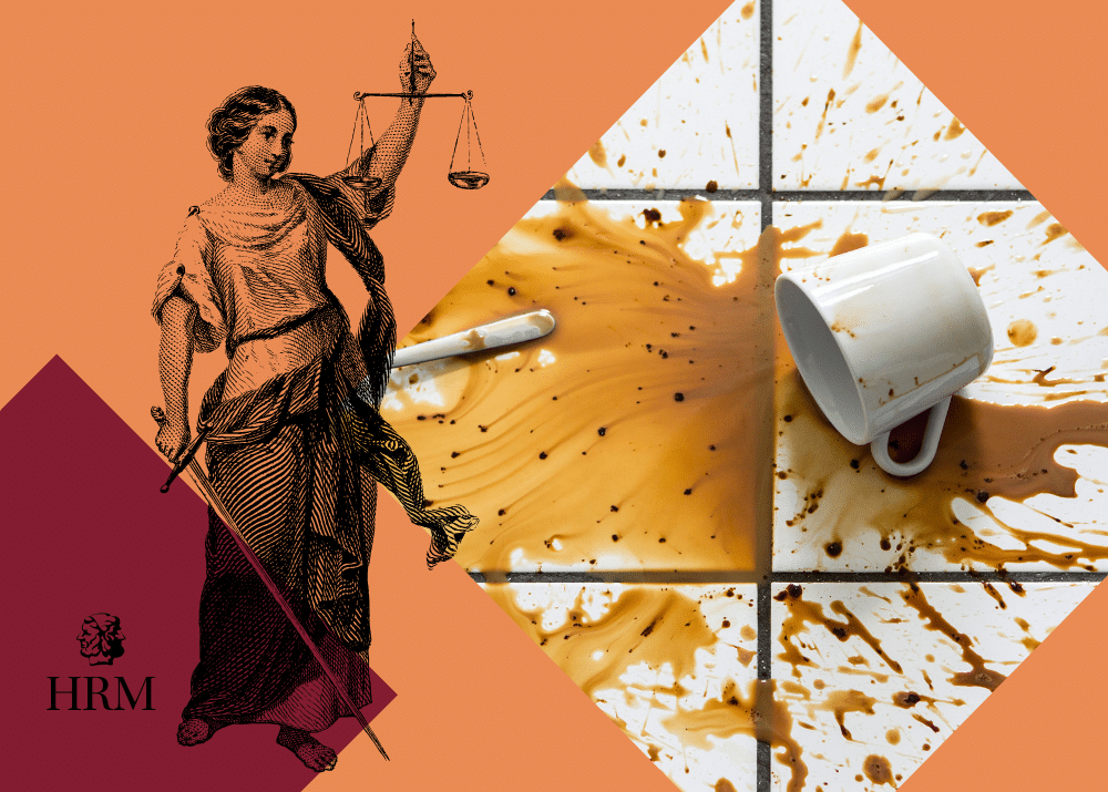 Eine umgekippte Tasse mit Kaffeeflecken auf Fliesen, daneben eine Statue der Justitia mit Waage und Schwert.