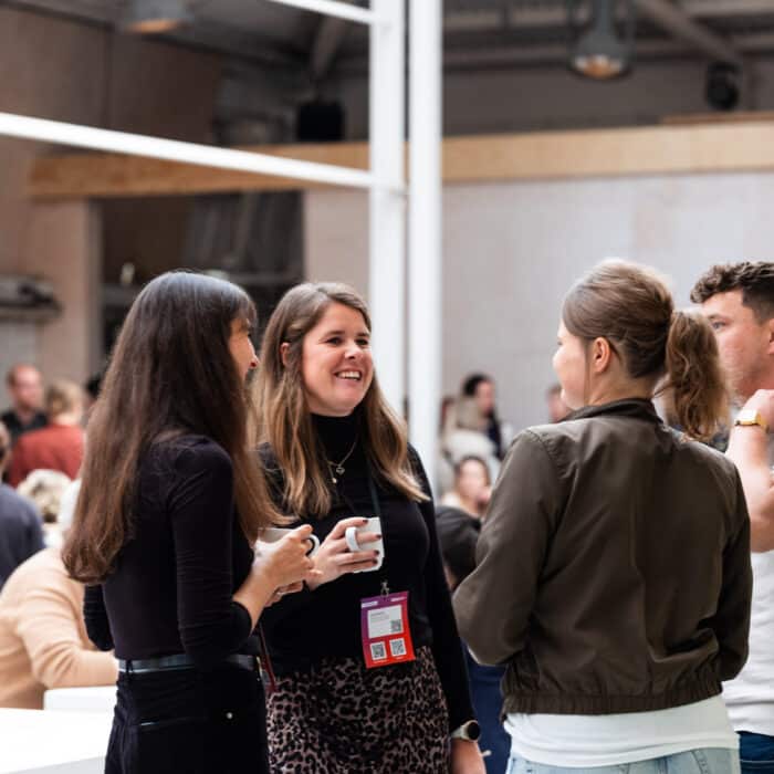 Vier Personen unterhalten sich in einem hellen, modernen Raum mit vielen weiteren Menschen im Hintergrund.