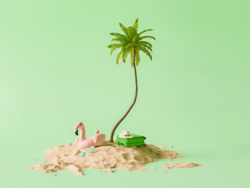 Ein pinker Flamingo und ein grüner Koffer stehen auf einem Sandhaufen unter einer Palme vor grünem Hintergrund.