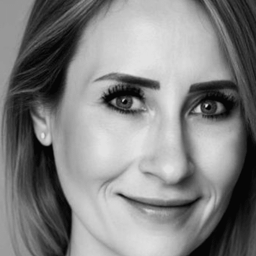 Porträt einer lächelnden Frau mit blonden Haaren und dezentem Make-up, vor neutralem Hintergrund.