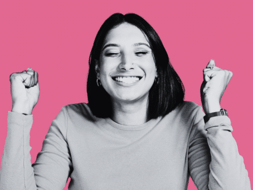 Lächelnde Frau mit kurzen Haaren, die die Fäuste in die Luft hebt, vor pinkem Hintergrund.