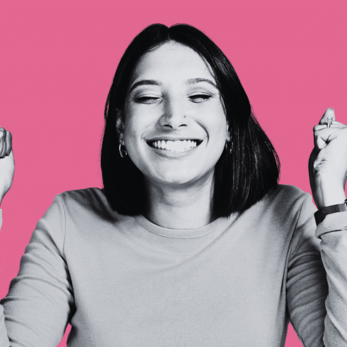 Lächelnde Frau mit kurzen Haaren, die die Fäuste in die Luft hebt, vor pinkem Hintergrund.