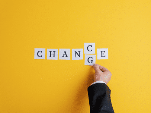 Hand hält Buchstaben auf weißen Karten, die das Wort "CHANGE" auf leuchtend gelbem Hintergrund bilden.
