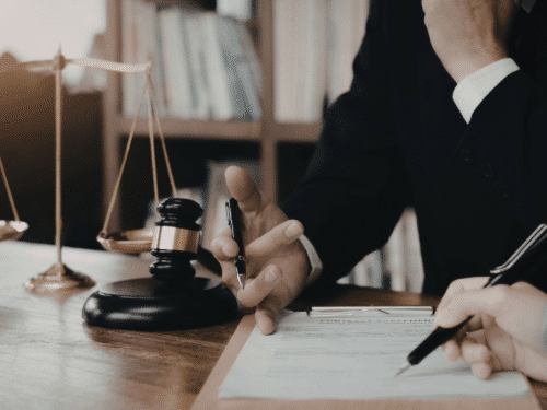 Rechtsanwalt diskutiert mit Klienten über Dokumente, im Hintergrund eine Waage der Gerechtigkeit.