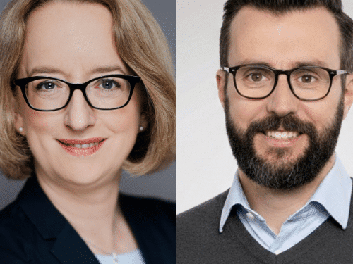 Zwei Personen mit Brille, eine Frau mit blonden, lockigen Haaren und ein Mann mit dunklem Bart und kurzen Haaren.