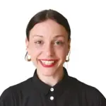 Porträt einer lächelnden Frau mit dunklen Haaren, die eine schwarze Bluse trägt und große Ohrringe hat.