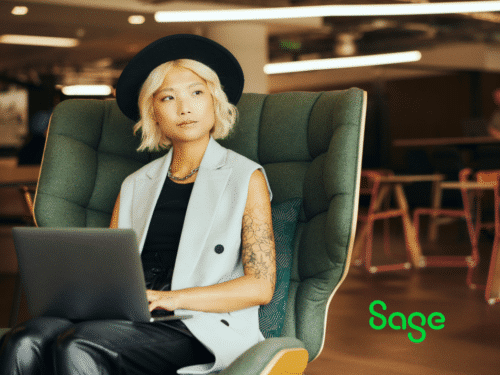 Junge Frau mit blonden, kurzen Haaren und Hut sitzt in einem modernen Sessel und arbeitet am Laptop.