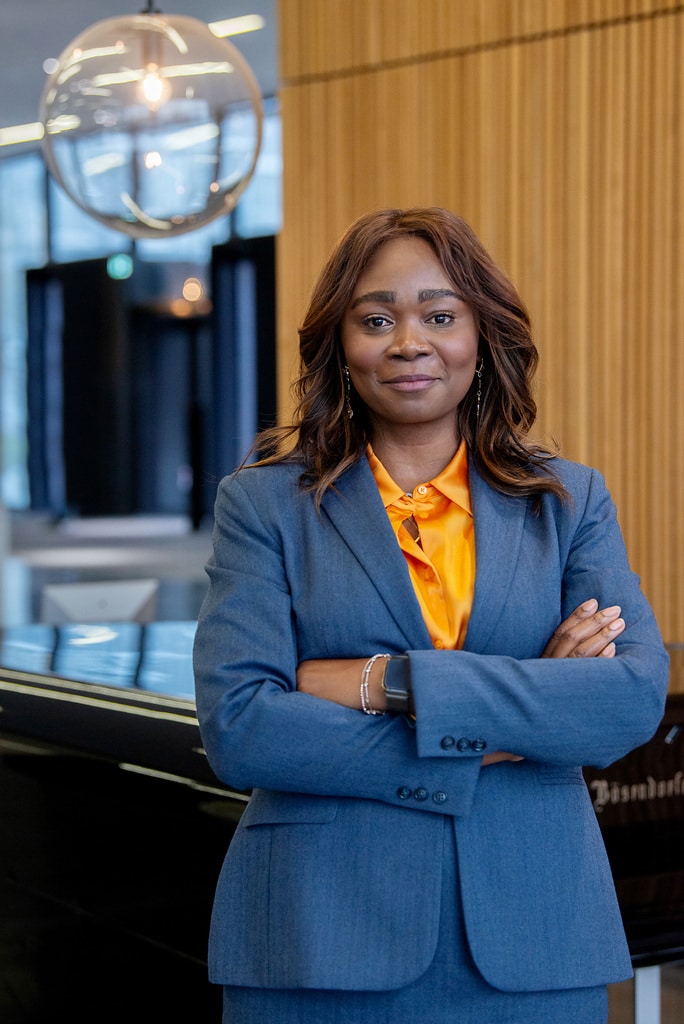 Yvonne Bettkober in einem blauen Anzug mit verschränkten Armen, lächelt vor modernem Hintergrund.