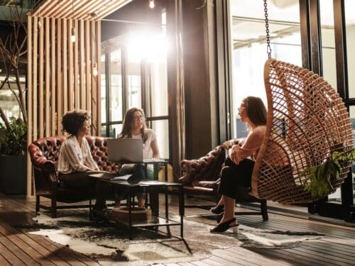 Junge Geschäftsleute arbeiten in einer modernen Bürolobby, sitzen auf Sofas und nutzen einen Laptop.