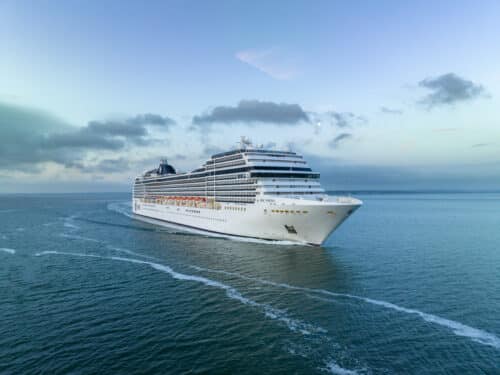 Aerial view of the MSC Poesia cruise ship arriving at Southampton port, surrounded by calm waters and a cloudy sky.