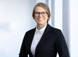 Hillert-Susan-sit-ppt Frau mit Brille und Blazer lächelt vor einem hellen Hintergrund.