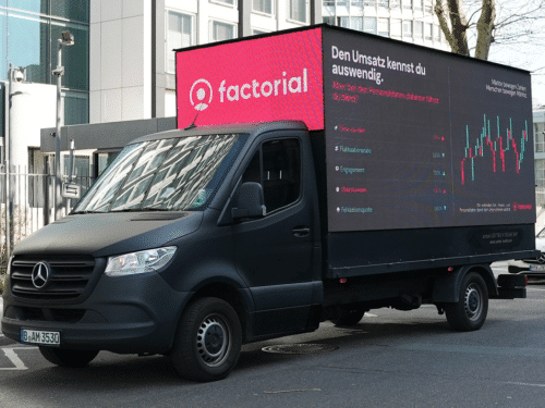 Schwarzer Lieferwagen mit digitalem Bildschirm, der Werbung für Factorial und Informationen zum Personalmanagement zeigt.