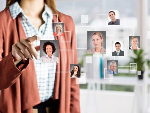 Person in einem blauen Hemd und braunem Blazer interagiert mit einem Netzwerk von Porträts in einem modernen Büro.