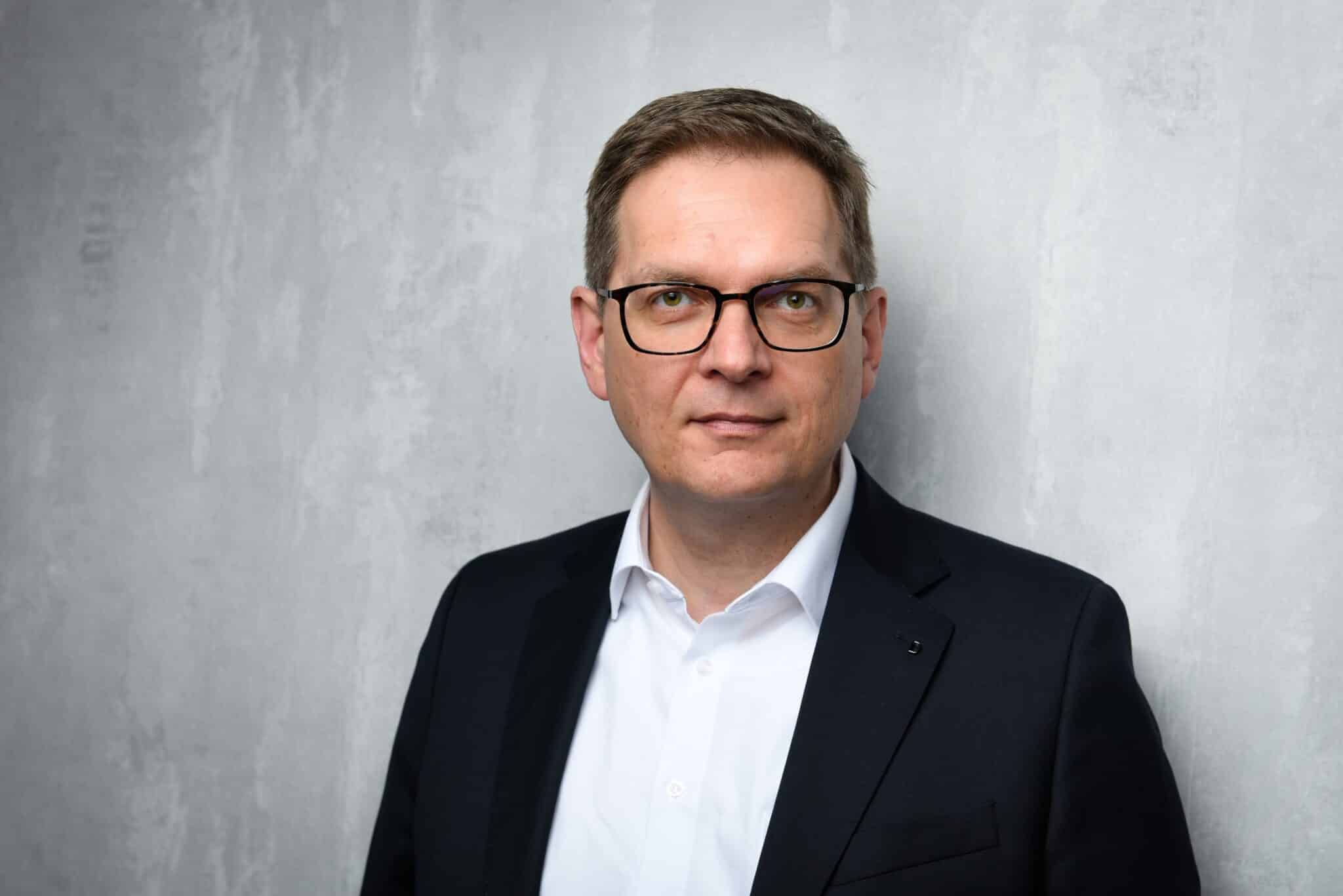 Porträt von Dr. Ulrich Braig in einem Anzug vor einer grauen Wand.