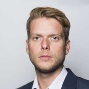 Frederik Nyga Porträt eines Mannes mit blonden Haaren, in Anzug und Hemd, vor neutralem Hintergrund.