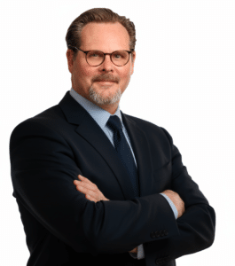 Frank A Walter c FA Walter Consulting Porträt eines Mannes mit Brille, in einem dunklen Anzug, mit verschränkten Armen vor einem weißen Hintergrund.