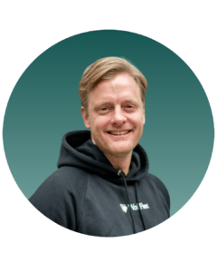 Lächelnder Mann mit blonden Haaren in schwarzem Hoodie, vor einem grünen Hintergrund in einem runden Rahmen.