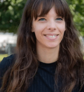 Porträt einer lächelnden Frau mit langen, braunen Haaren, die ein schwarzes Oberteil trägt, vor einem grünen Hintergrund.