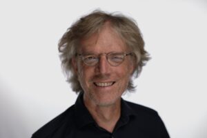 eichhorst c privat Porträt eines lächelnden Mannes mit blonden, lockigen Haaren und Brille, vor einem hellen Hintergrund.