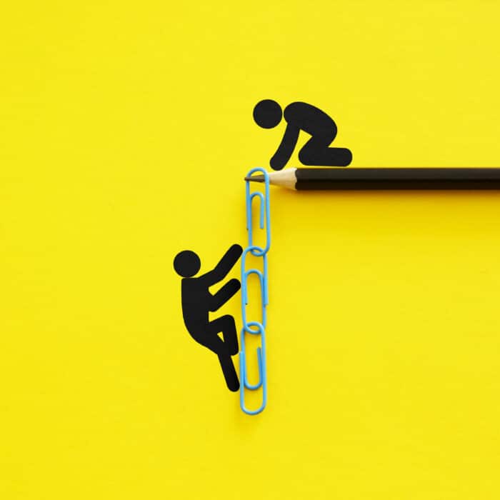 Papierclip-Kettenleiter auf gelbem Hintergrund, mit Figuren, die Unterstützung und Teamarbeit symbolisieren.