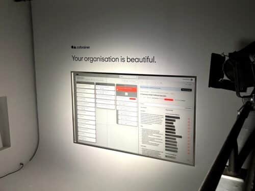 Ein Bildschirm zeigt eine Benutzeroberfläche mit Text und Listen, darüber steht der Schriftzug: "Your organisation is be...