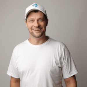 Lächelnder Mann in weißem T-Shirt und Baseballcap vor neutralem Hintergrund.