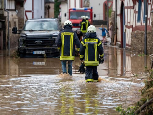 Feuerwehrleute gehen durch überflutete Straßen in einem beschädigten Ort nach einem Unwetter in Rheinland-Pfalz.