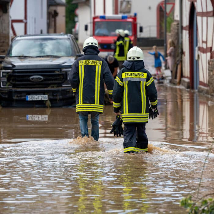 Feuerwehrleute gehen durch überflutete Straßen in einem beschädigten Ort nach einem Unwetter in Rheinland-Pfalz.