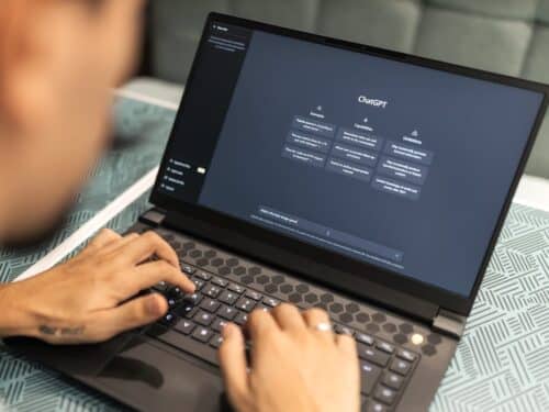 Person tippt auf Laptop, der eine Benutzeroberfläche mit verschiedenen Optionen anzeigt, auf einem Tisch mit geometrische...
